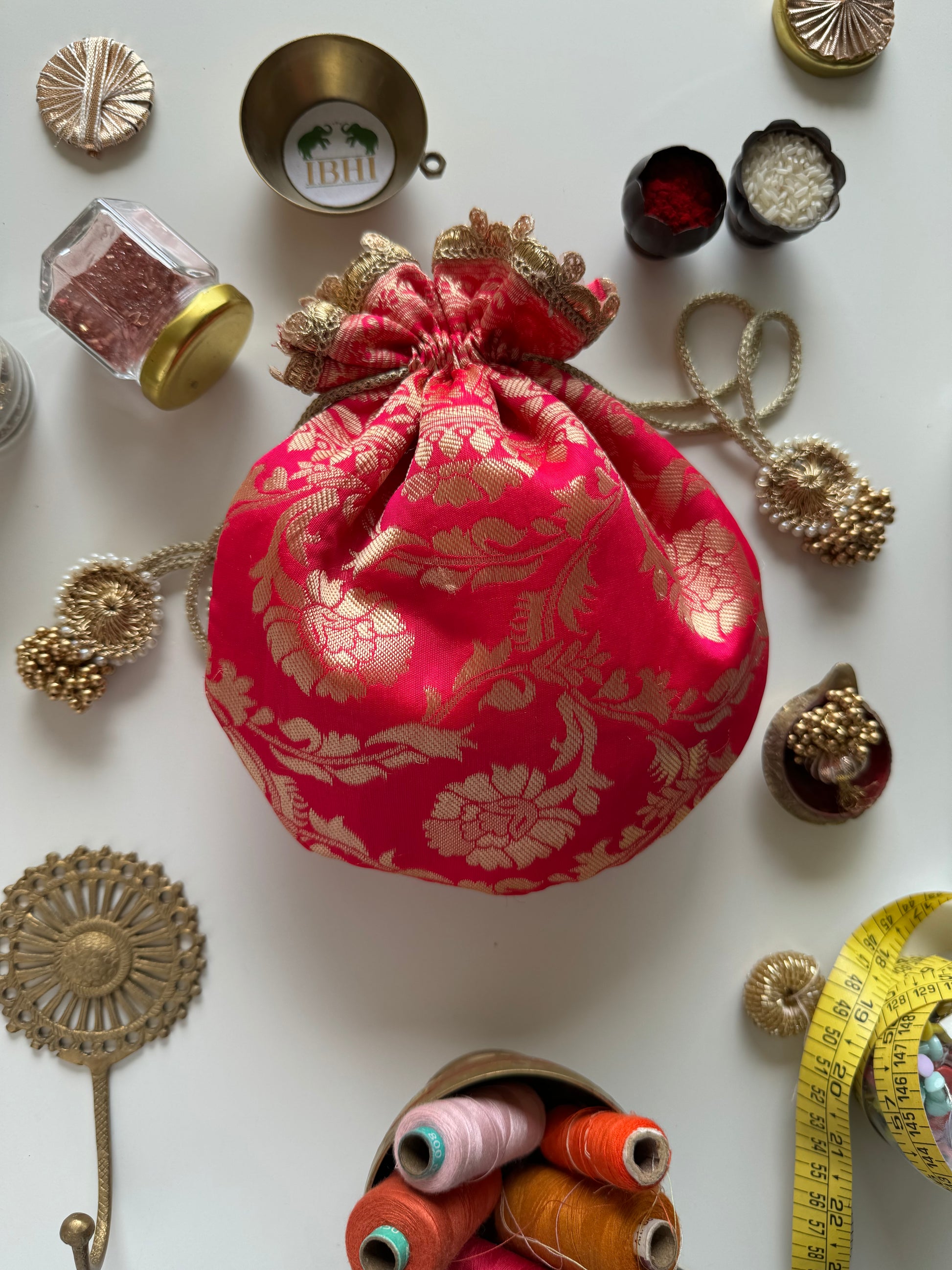 Handcrafted pink Banarasi potli bag with golden zari floral motifs, lace border, and drawstring tassels – ideal for weddings and festive gifting.