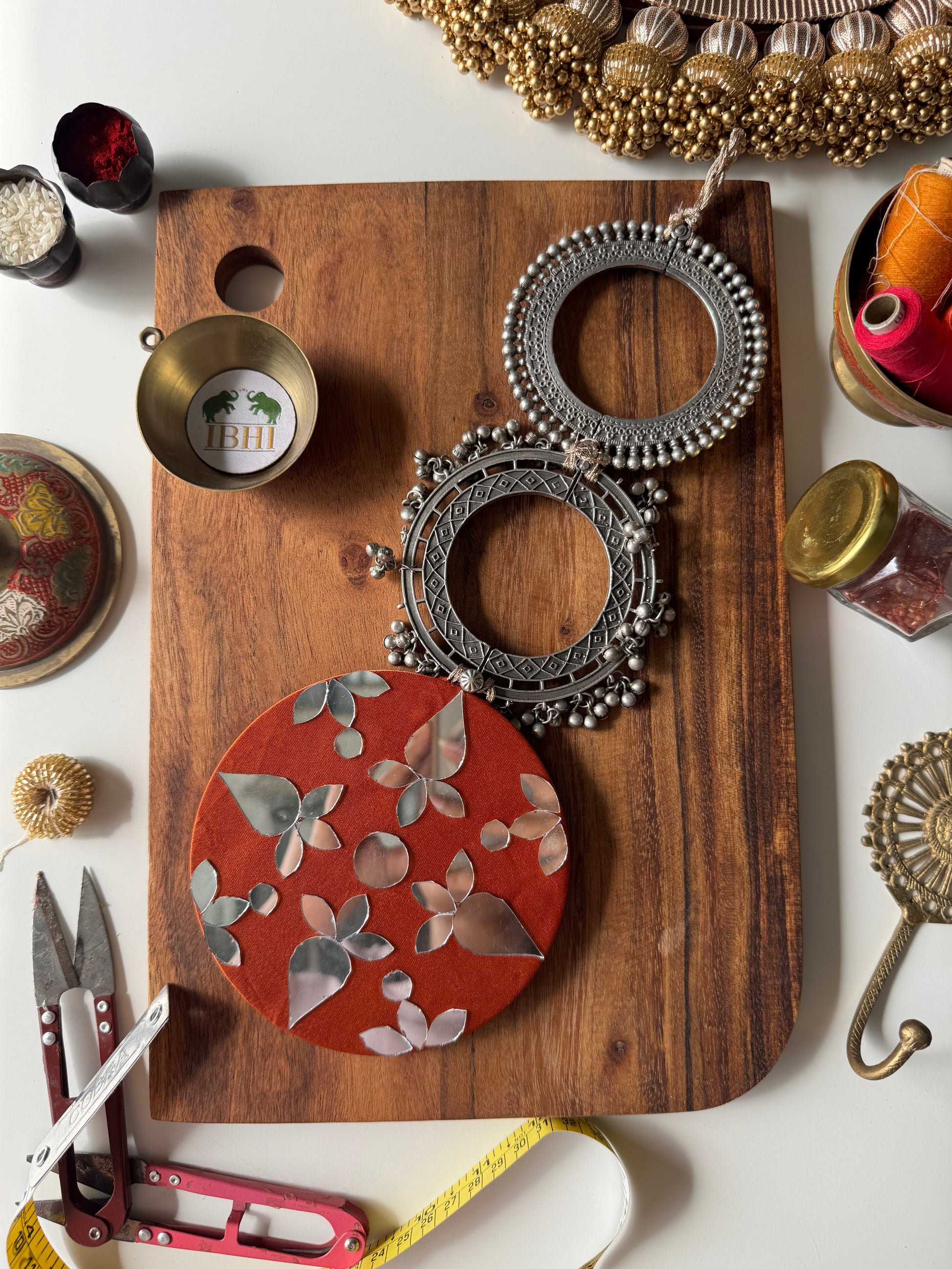 Handmade wall hanging with brass bangles, mirror art, and ghungroo detailing on vermillion silk – Shubhra Chakra by IBHI