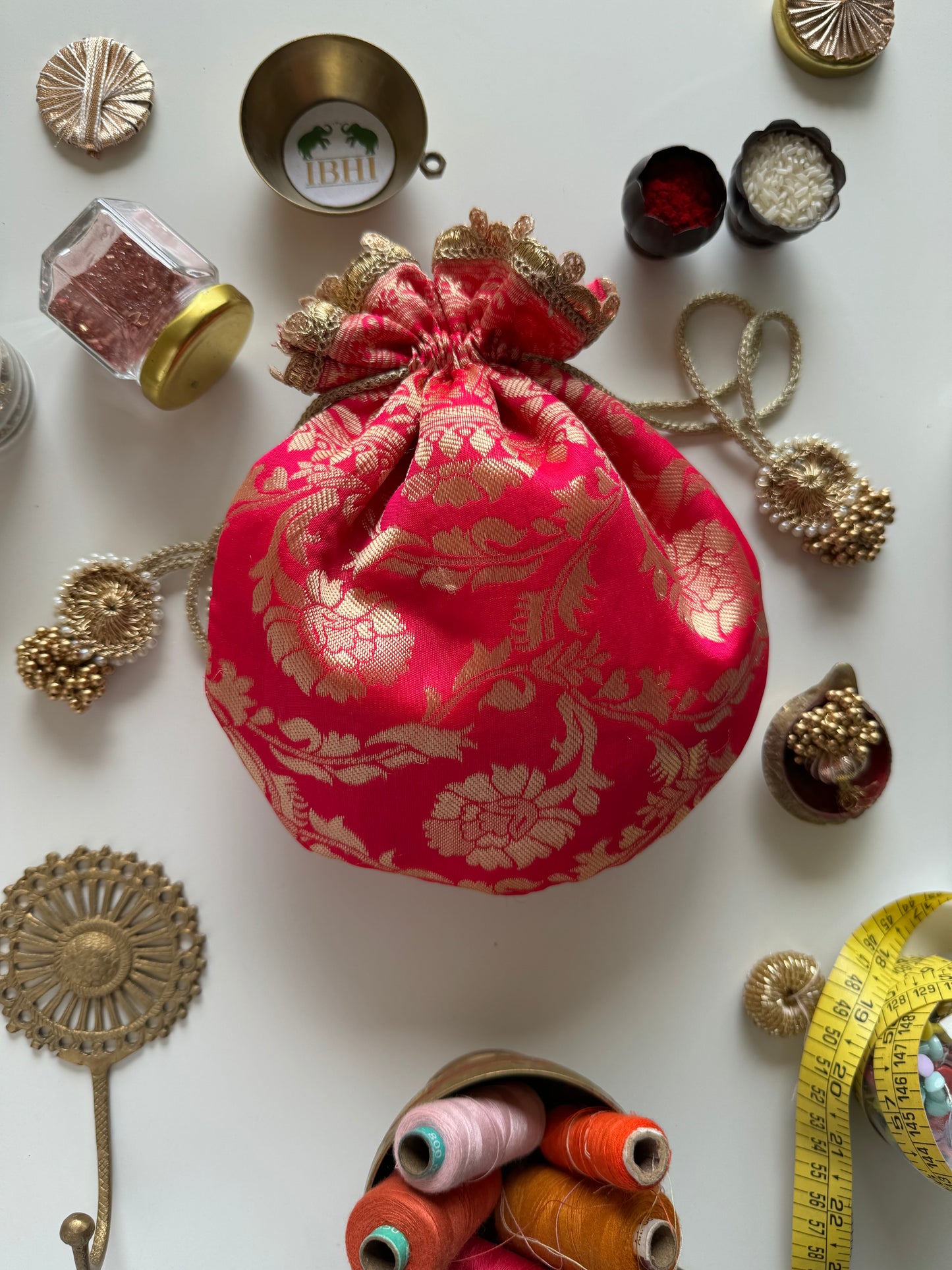 Handcrafted pink Banarasi potli bag with golden zari floral motifs, lace border, and drawstring tassels – ideal for weddings and festive gifting.


