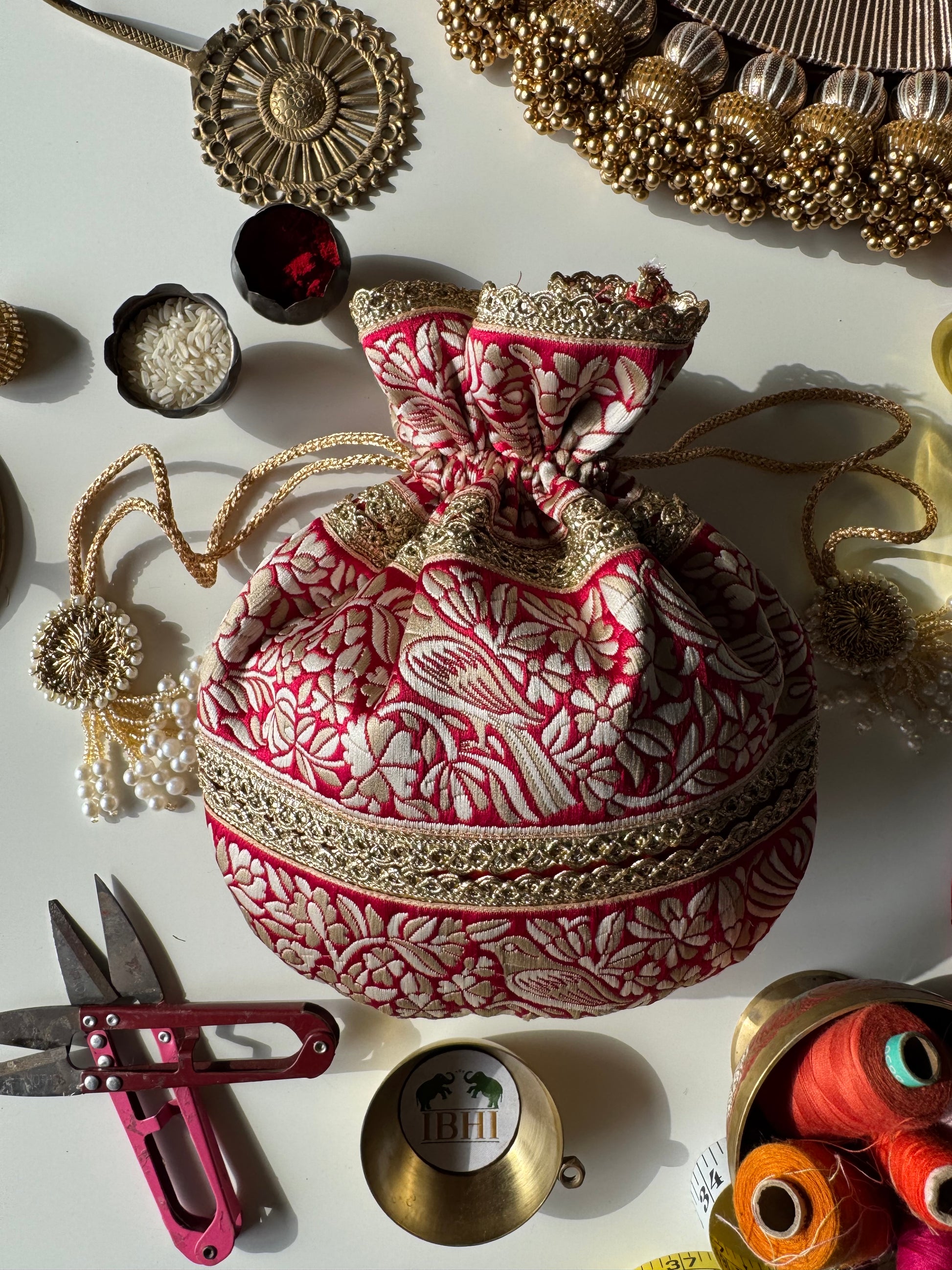 PakshiRaag potli bag featuring Parsi Gara bird embroidery on rich fabric with gold border and tassels – ideal for weddings and festive return gifts.

